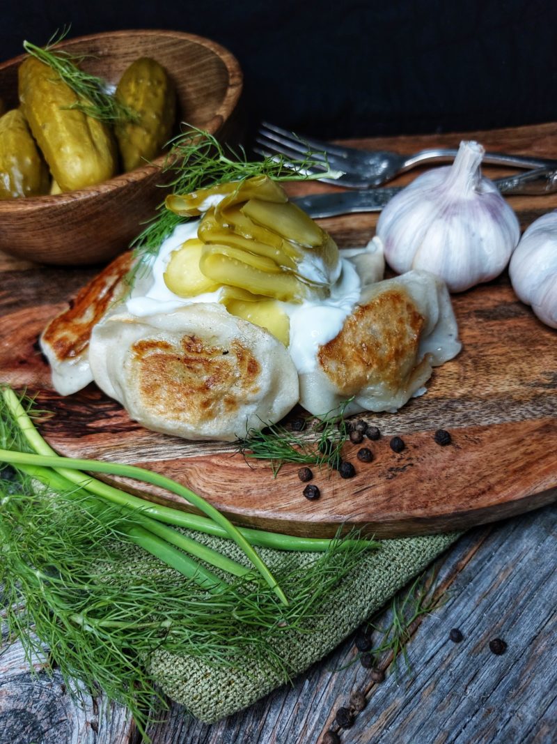 Dill Pickle Pierogi on a cutting board, topped with sliced pickles