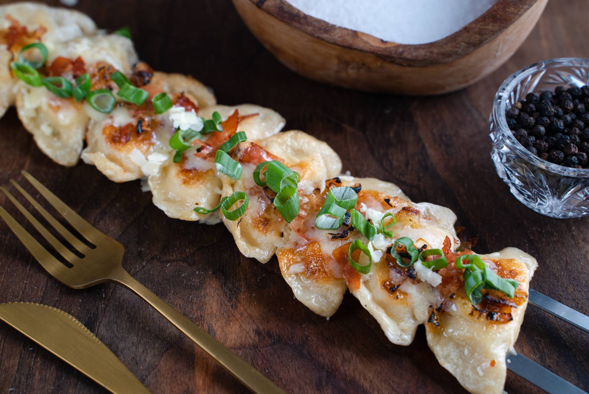 Fried pierogi on a skewer topped with bacon and green onions